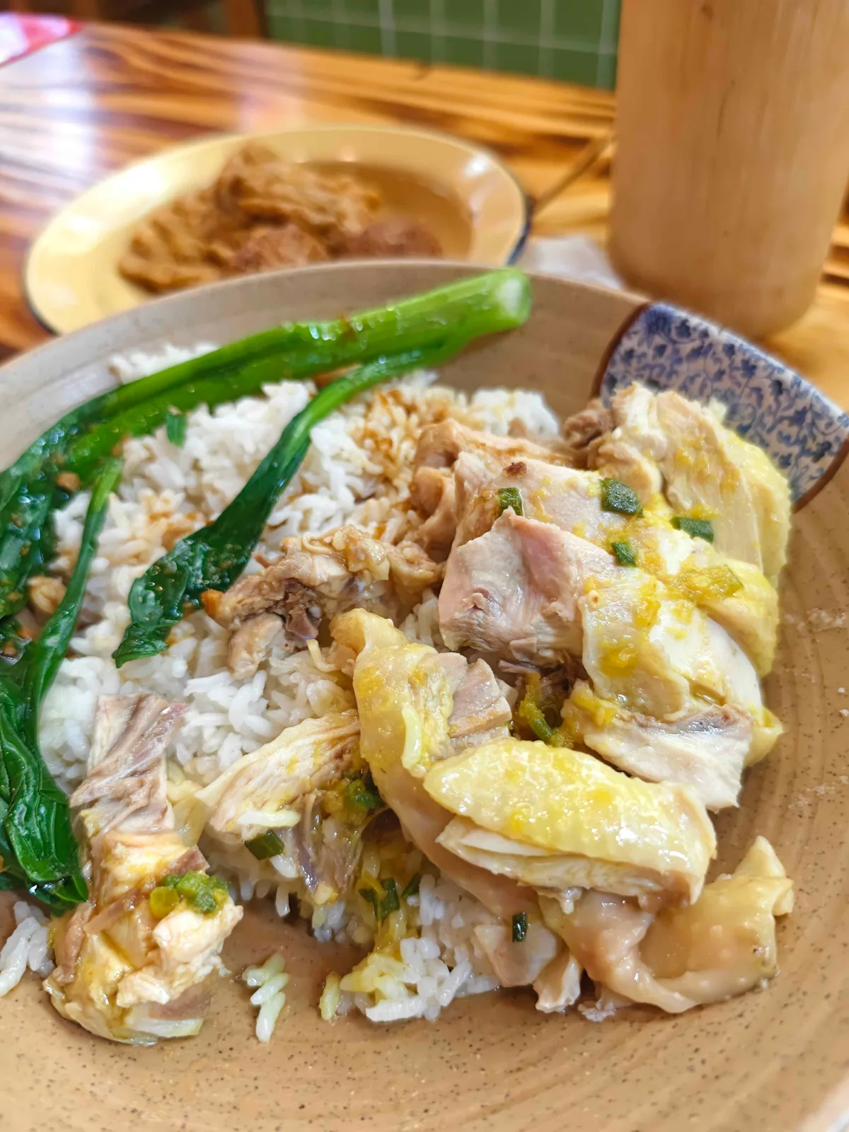 A ceramic plate of poached chicken over rice with ginger-scallion oil and blanched greens, shot from above.