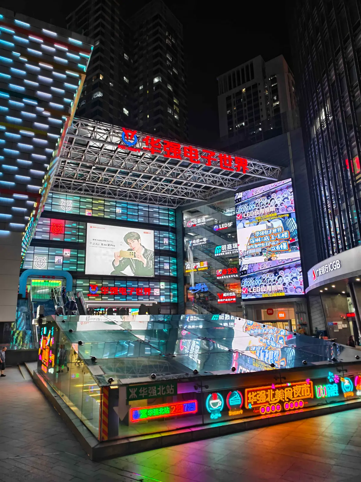 The lit entrance of Huaqiang Electronic World at night, its LED-clad facade and screens above the Huaqiangbei metro entrance.