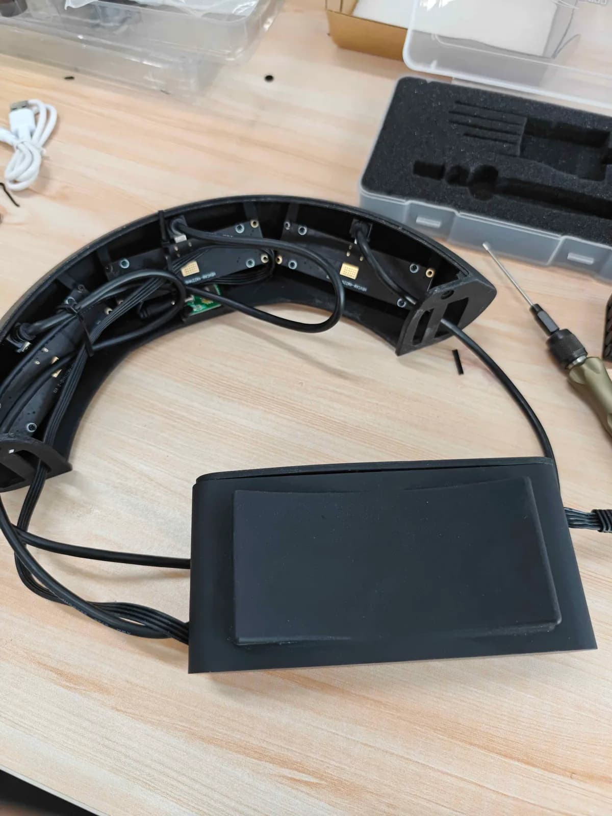 An opened AR headset on a workbench with its curved headband unscrewed, internal ribbon cables exposed, next to a foam-lined tool case.