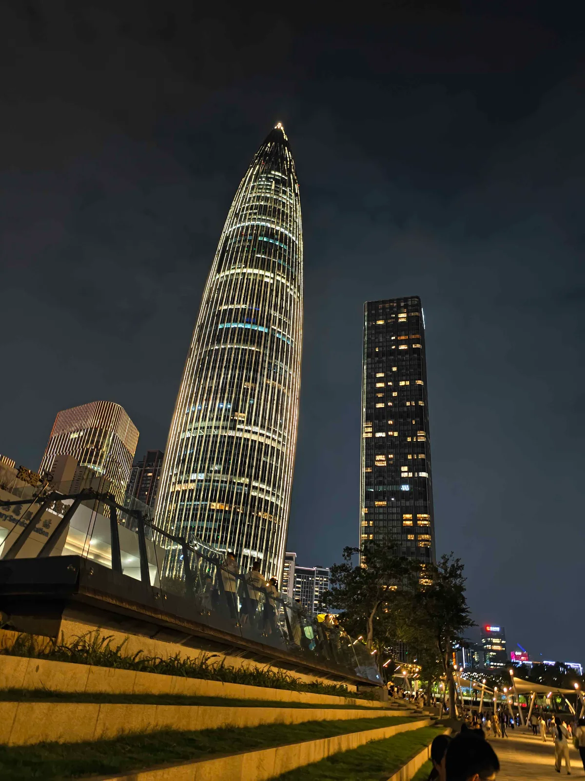 A Shenzhen tower lit white against the night sky, seen past a raised pedestrian walkway