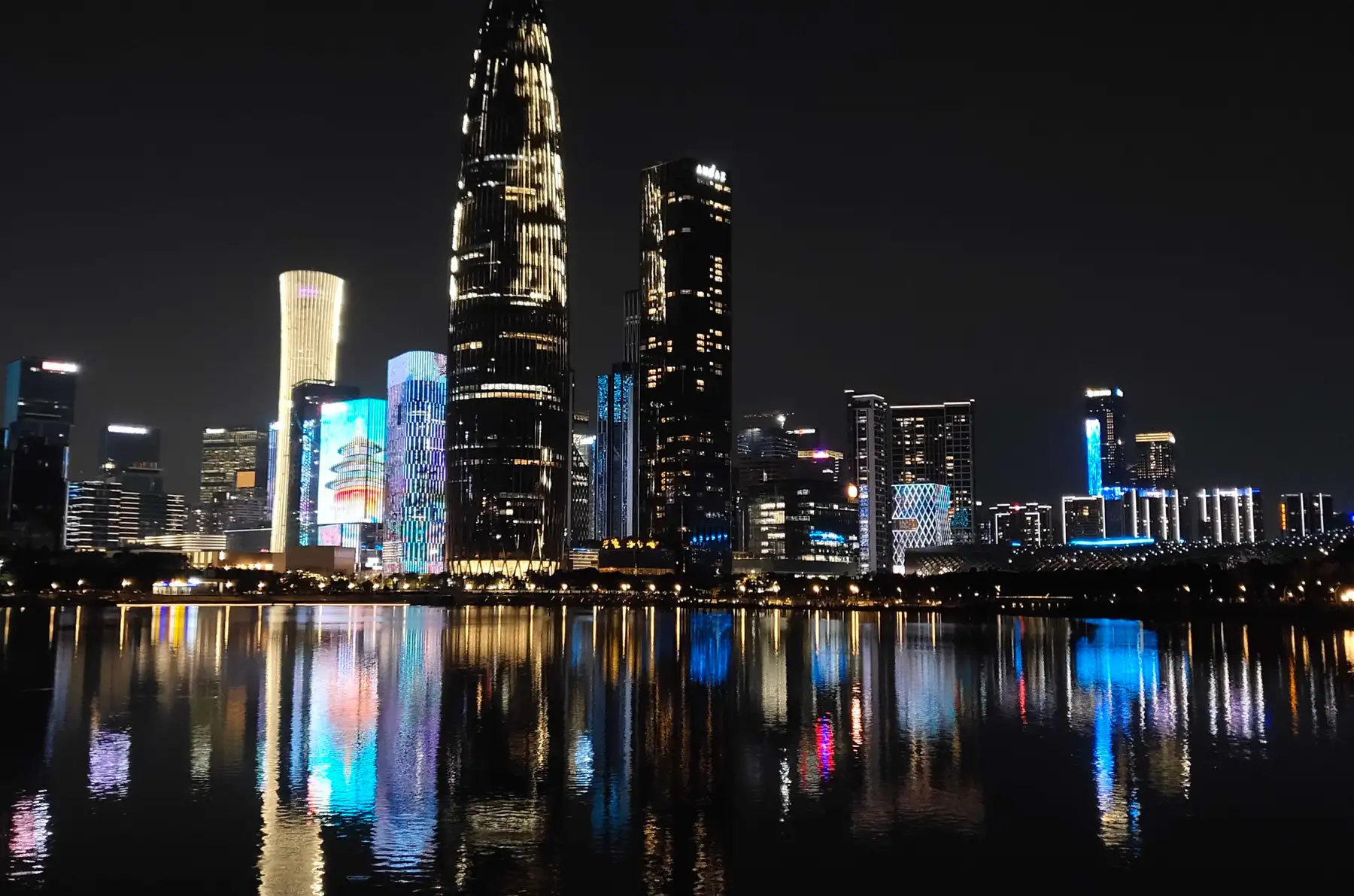 Nanshan's skyline lit up at night across Shenzhen Bay, the towers mirrored in still water